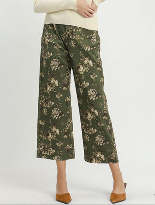 A model wearing olive green wide-leg cropped pants with a beige floral print, styled with a cream turtleneck sweater and brown pointed-toe heels, against a plain white studio background.